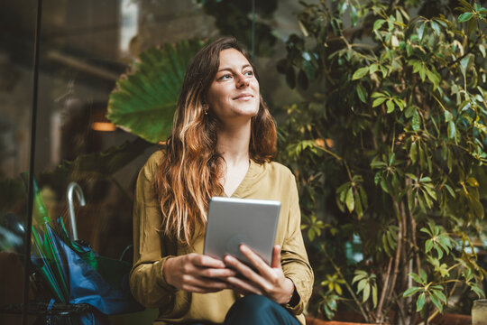 Thoughtful young woman sitting with tablet PC in cafe