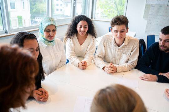 Students sitting with hands clasped around table in classroom