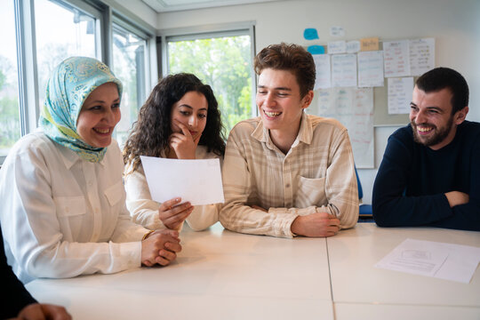 Woman showing document to friend sitting with students in classroom