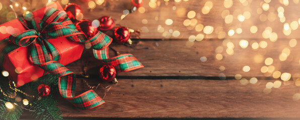 Hands in cozy sweater opening christmas gift with red bow on background of christmas tree with lights. Stylish female holding present with red ribbon in festive room close up. Merry Christmas!