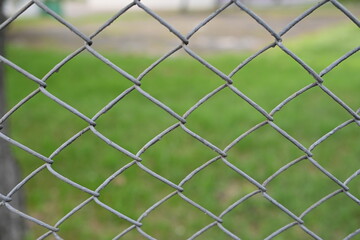 green mesh fence on the background of green nature, iron fence mesh close up, blurred city, city...