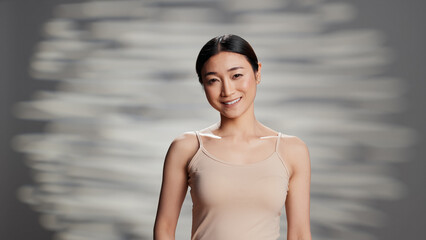Fototapeta na wymiar Young asian model promoting self love with new products for skincare campaign, advertising beauty cosmetics and routine. Cheerful radiant girl with luminous bare skin posing in studio.