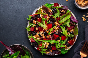 Vegan salad with beet, dried plums, arugula, swiss chard and walnuts, black stone table background. Fresh useful vegetarian dish for clean eating