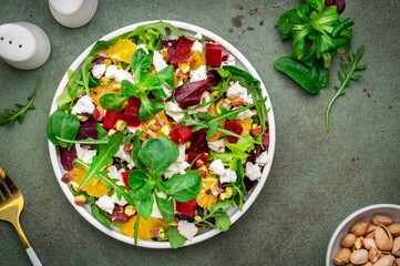 Beet and feta cheese salad with arugula, lettuce, orange and pistachios on green table. Fresh useful dish for healthy eating