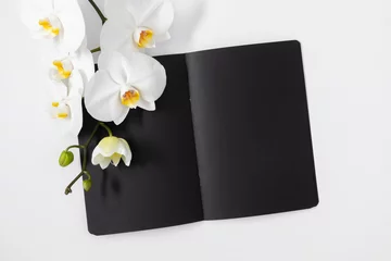 Foto op Canvas Flat lay, top view of open black notebook and white orchid branch on white background, copy space © prime1001