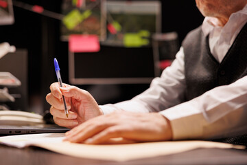 Senior police officer writing missing person case report, working overhours at criminal case in...