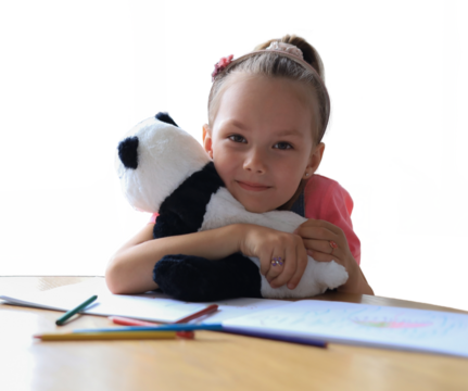 Excited child looking at camera hugging her toy panda while sitting on a transparent background