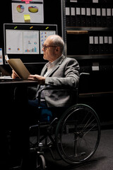 Senior businessman executive in wheelchair checking accountancy budget plan data paperwork. Experienced bureaucratic employee in depository filled with document folders chart reports