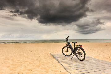 Obraz premium Bike parked on the beach of the Curonian Spit under dark clouds during a bike tour of Poland