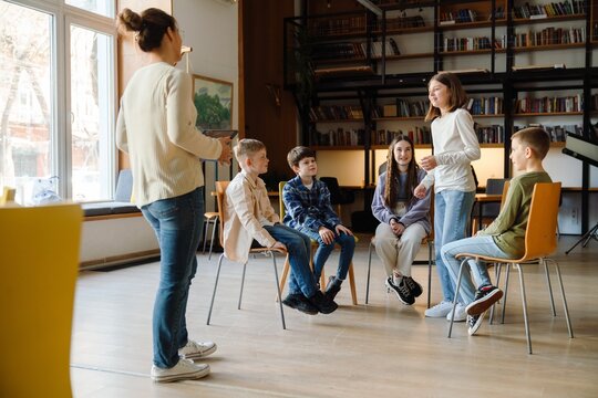 Group of school children discussing something with teacher in library