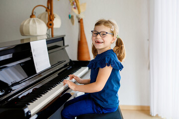 Beautiful little preschool girl playing piano at music school. Cute child having fun with learning...