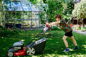 Happy preteen kid boy with lawn mower. Portrait of smiling teenager child working in garden,...