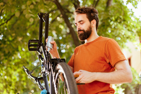 Sporty dedicated man utilizing specialized lubricant to grease his bicycle chain. The image displays caucasian man skillfully oiling his bike's chain ring for a seamless cycling experience.