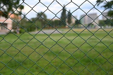 green mesh fence on the background of green nature, iron fence mesh close up, blurred city, city fences concept