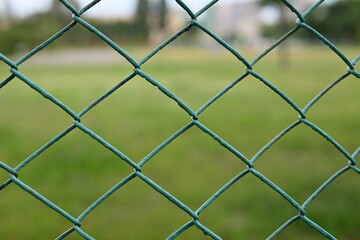 green mesh fence on the background of green nature, iron fence mesh close up, blurred city, city fences concept