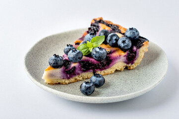 A piece of blueberry shortcake with a mint leaf, scattered blueberries, horizontal shot, on a white background.