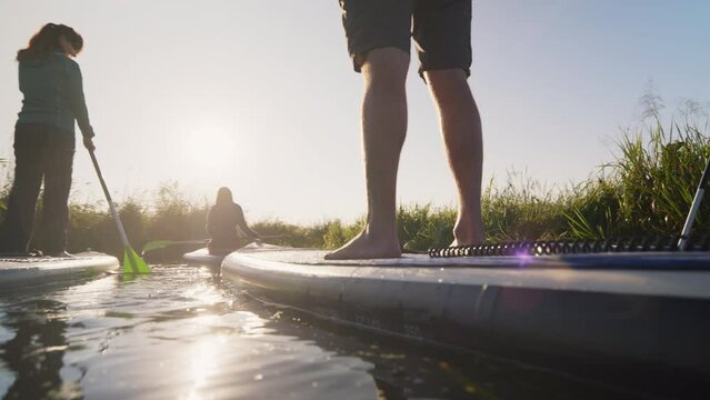 Group of people riding paddleboards in narrow river during sunny morning