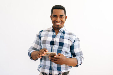 Studio portrait of cheerful african american man in plaid shirt holding mobile smartphone standing on white isolated background, smiling looking at camera with friendly expression.
