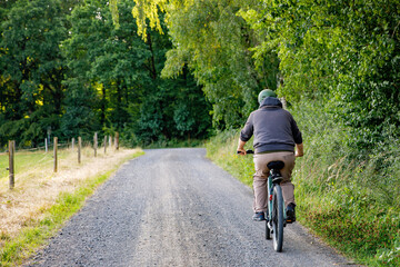 Naklejka premium Mountain biker riding on bike in summer forest landscape. Active middle-aged man cycling on bicycle, sports and leisure activity.