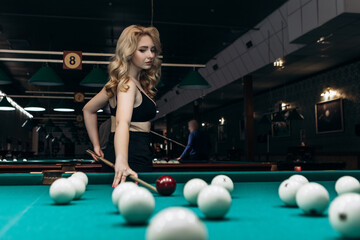 Blond woman playing enjoying billiard, hold cue hit white billiard balls on table with green...