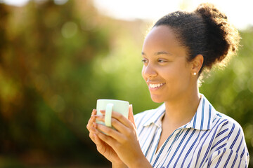 Happy black woman holding coffee mug contemplating