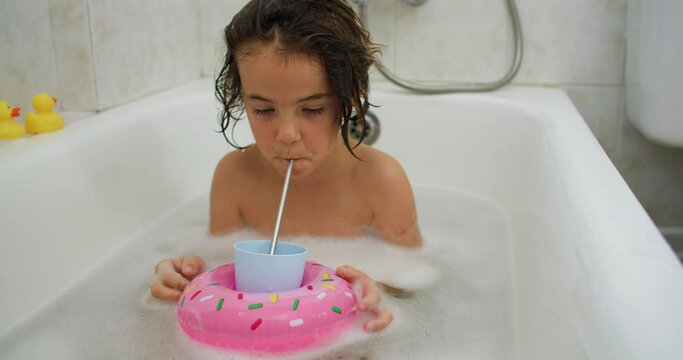 Baby girl takes a bath and plays in the water. The child drinks a cocktail in the bathroom. High quality 4k footage