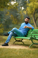 Obraz premium Young Indian man sitting at park and looking time in wristwatch.