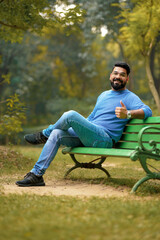 Young and confident indian man showing thumps up at park.