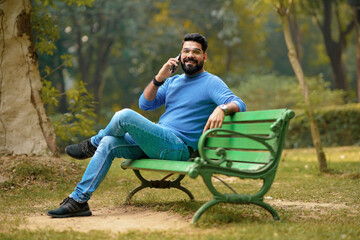 Young indian man talking on smartphone at park.