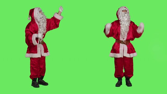 Santa choirmaster conducting band, conductor in winter seasonal costume accompany choir over full body greenscreen backdrop. Character pretends to be musical director, musician in studio.
