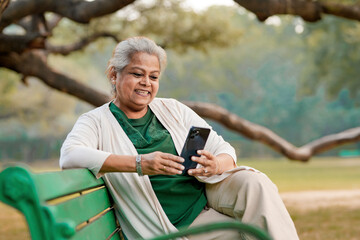 Indian senior woman using smartphone at park.