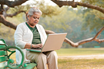 Fototapeta premium Indian senior woman using laptop at park.