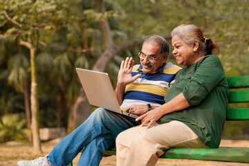 Fototapeta na wymiar indian senior couple sitting at park and using laptop