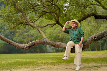 Happy senior indian woman wearing hat and sitting on tree branch at in the green forest nature.