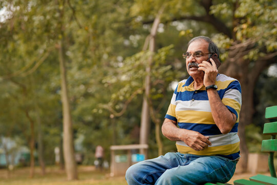 Old Indian man talking on smartphone at park.