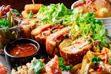 fast food set on plate. sandwich, potato chips, french fries, chicken wings, fried cheese and more on table.
