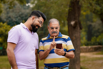 Indian old man showing some detail in smartphone to his son at park.