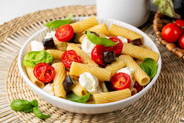 Italian pasta rigatoni with roasted eggplant, tomato, mozzarella bufala cheese and basil leaves. Close-up.