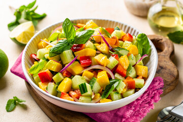 A bowl with healthy fresh mango salad made with red bell pepper, cucumber, red onion, fresh mint,...