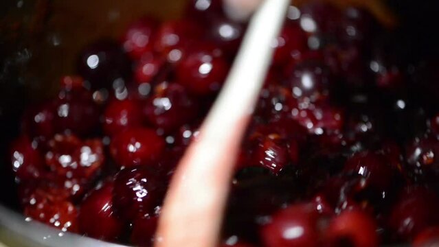 Mixing with a spoon, cooked cherry fruit jam in a pot. Mixing the cherries. 