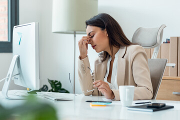 Stressed overwhelmed businesswoman working with computer while having headache in the office