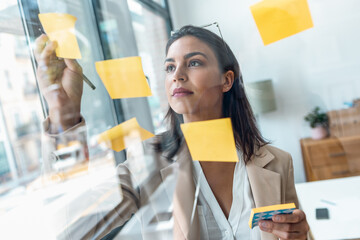 Elegant beautiful businesswoman working on wall glass with post it stickers in the office
