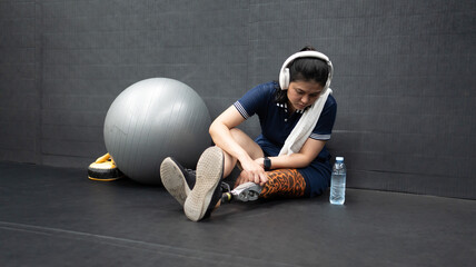 Asian woman with prosthetic leg sits isolated in gym. Young girl with foot prosthesis physical...