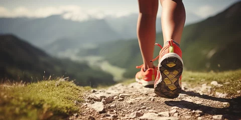 Foto op Plexiglas Bosweg Men's legs with sports shoes and a backpack run along a mountain path.