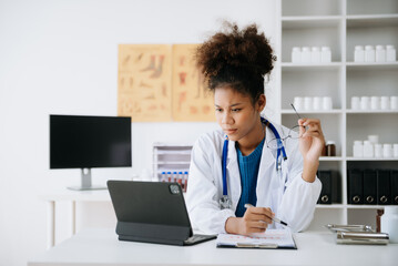 Beautiful physician doctor sit on table in office hospital. Attractive therapist female practitioner pharmacist smile and use tablet and laptop in hospital.after success work from treatment.