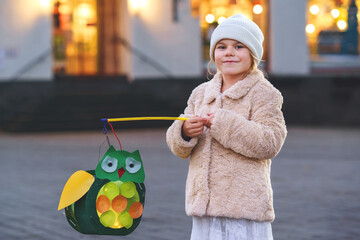 Little preschool kid girl holding selfmade traditional owl lanterns with candle for St. Martin...