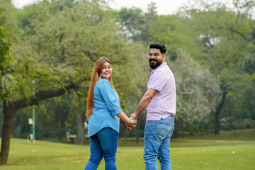 young indian couple holding hand each other and walking in park