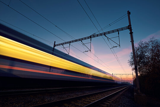 Railway at beautiful dawn. Long exposure of train on railroad track. Moving modern intercity passenger train..