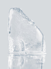 Piece of crystal clear crushed ice block, isolated on a light gray reflective surface.