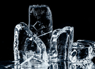 A group of crystal clear crushed ice pieces on a reflective surface on black background.